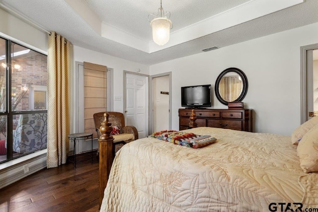 bedroom with dark wood-type flooring, a raised ceiling, visible vents, and a textured ceiling