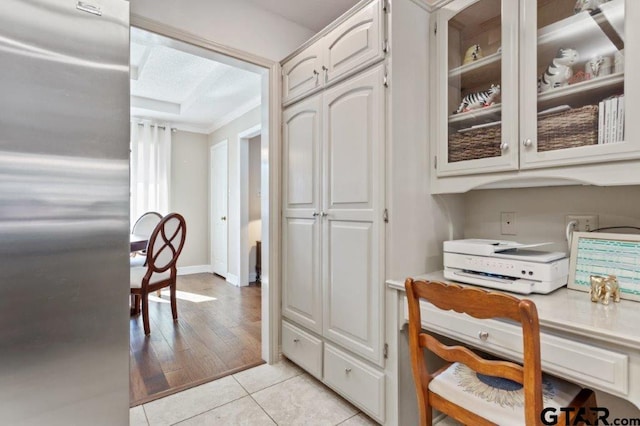 kitchen featuring light tile patterned floors, light countertops, glass insert cabinets, white cabinetry, and stainless steel fridge