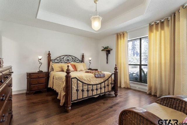 bedroom with a textured ceiling, a tray ceiling, and dark wood-type flooring