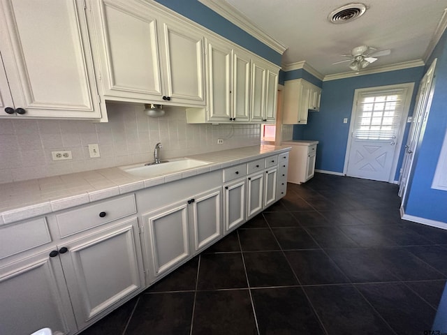 kitchen with tasteful backsplash, crown molding, sink, tile counters, and ceiling fan