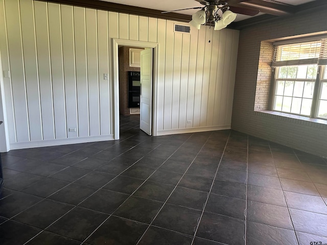 tiled empty room with ornamental molding, wood walls, beamed ceiling, ceiling fan, and brick wall