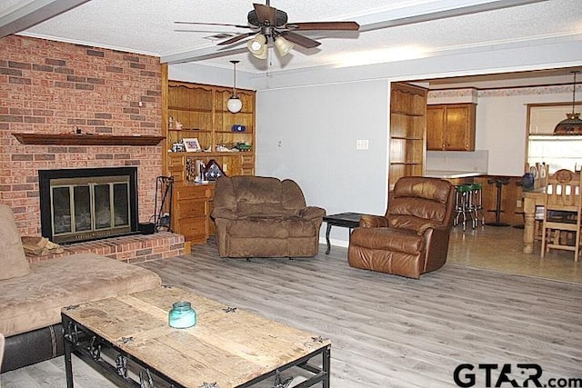 living room featuring a brick fireplace, light hardwood / wood-style flooring, a textured ceiling, and ceiling fan