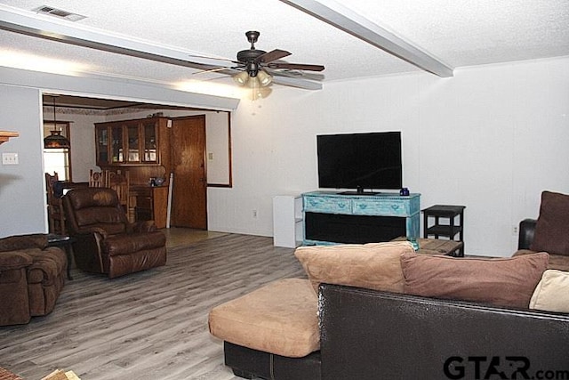 living room featuring a textured ceiling, hardwood / wood-style floors, beamed ceiling, and ceiling fan