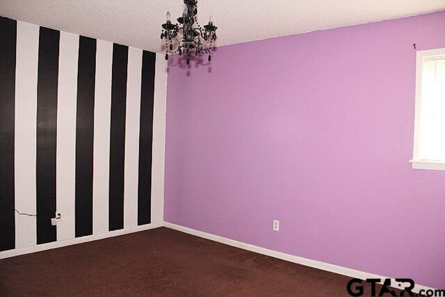 spare room featuring plenty of natural light, a textured ceiling, carpet floors, and a notable chandelier