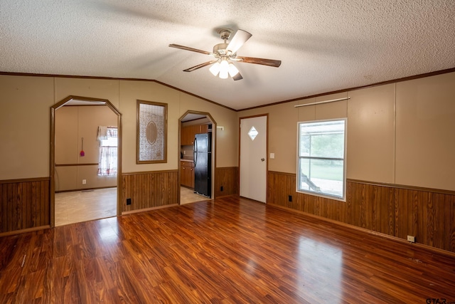 interior space with lofted ceiling, a textured ceiling, hardwood / wood-style flooring, wooden walls, and ceiling fan