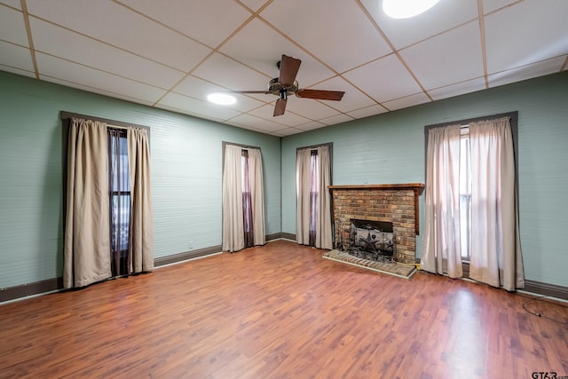 unfurnished living room with a drop ceiling, hardwood / wood-style floors, ceiling fan, and a brick fireplace