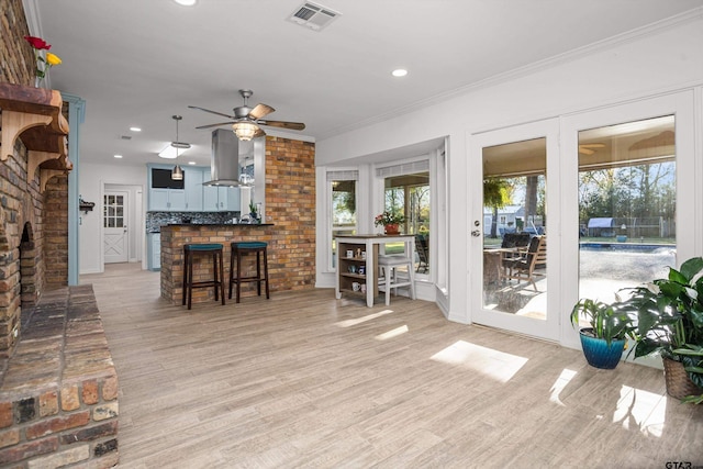 living room with ceiling fan, a fireplace, ornamental molding, and light wood-type flooring