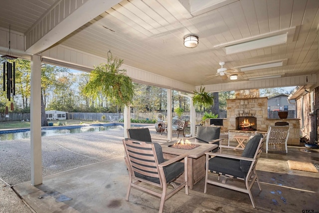 view of patio featuring an outdoor stone fireplace, ceiling fan, a fenced in pool, and an outdoor fire pit