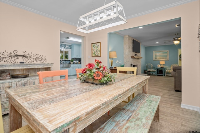 dining area featuring a stone fireplace, crown molding, light hardwood / wood-style flooring, and ceiling fan