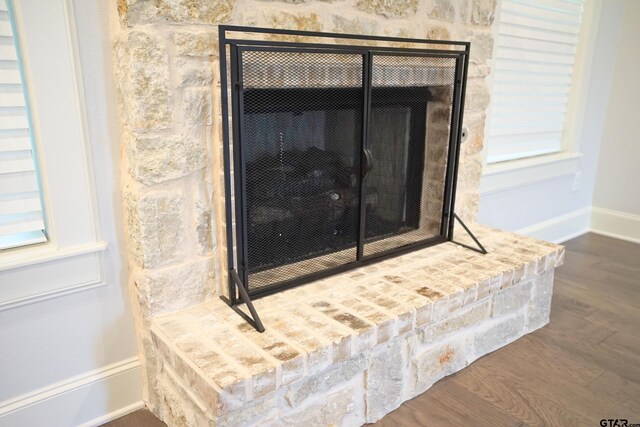 room details featuring baseboards, a fireplace with raised hearth, and wood finished floors