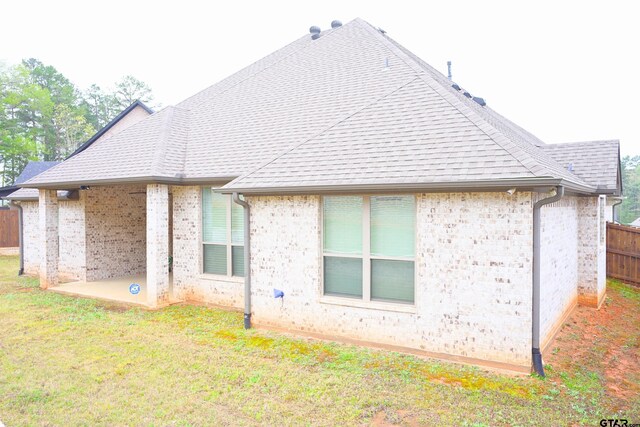 rear view of property featuring a lawn, fence, brick siding, and a patio