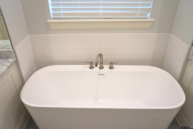 bathroom featuring a freestanding bath, vanity, a wainscoted wall, and tile walls