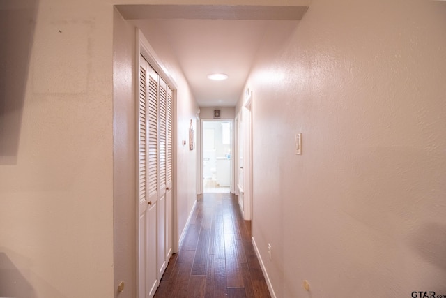 corridor with dark wood-style floors, a textured wall, and baseboards