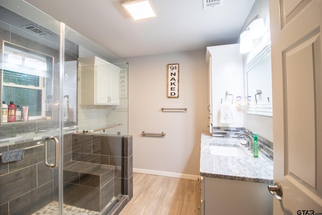 full bathroom with visible vents, vanity, a shower stall, wood finished floors, and baseboards