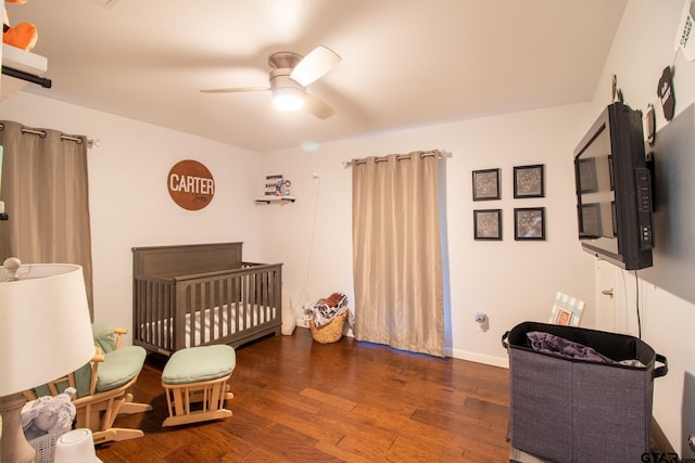 bedroom with a nursery area, ceiling fan, baseboards, and dark wood-type flooring