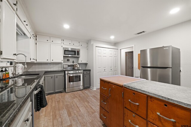 kitchen featuring stainless steel appliances, backsplash, sink, white cabinets, and light hardwood / wood-style flooring