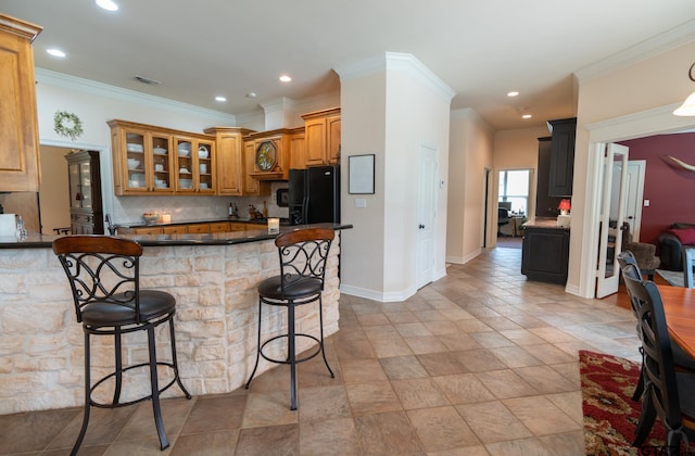 kitchen with black fridge, kitchen peninsula, ornamental molding, backsplash, and a breakfast bar