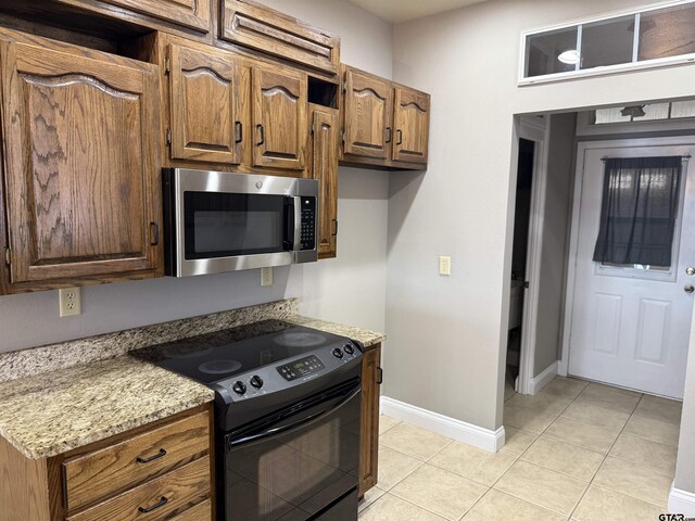 kitchen with stainless steel microwave, baseboards, light tile patterned floors, light stone counters, and black / electric stove