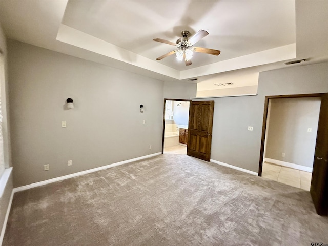 empty room with visible vents, a ceiling fan, a tray ceiling, baseboards, and light colored carpet