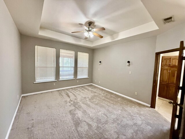 empty room with light carpet, visible vents, baseboards, and a tray ceiling