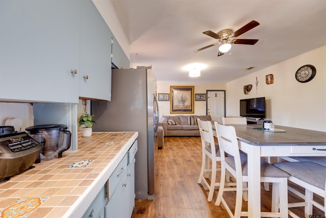 kitchen featuring ceiling fan, stainless steel refrigerator, tile counters, and light wood-type flooring