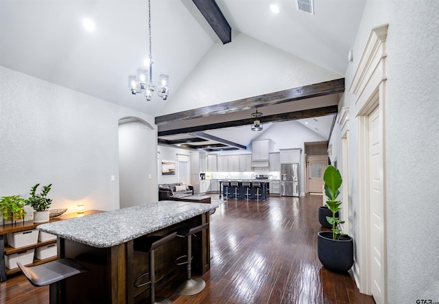 kitchen with pendant lighting, vaulted ceiling with beams, a kitchen bar, a center island, and stainless steel fridge with ice dispenser