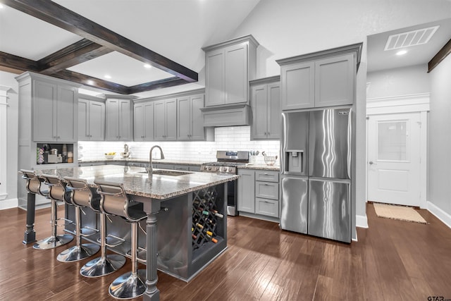 kitchen featuring sink, a breakfast bar, beam ceiling, stainless steel appliances, and light stone counters