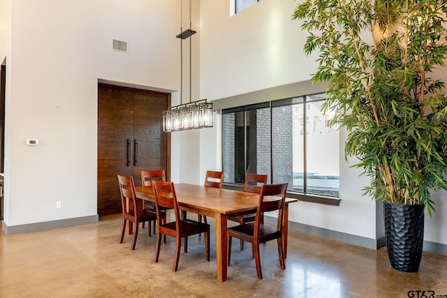 dining space featuring concrete flooring, a towering ceiling, visible vents, and baseboards