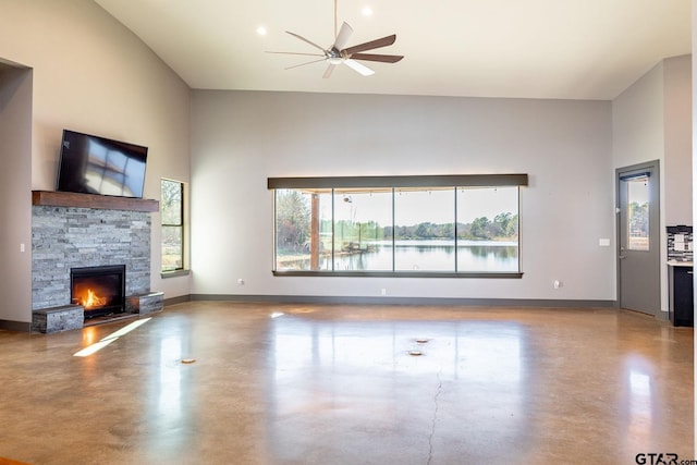 unfurnished living room featuring a ceiling fan, concrete floors, a stone fireplace, and baseboards