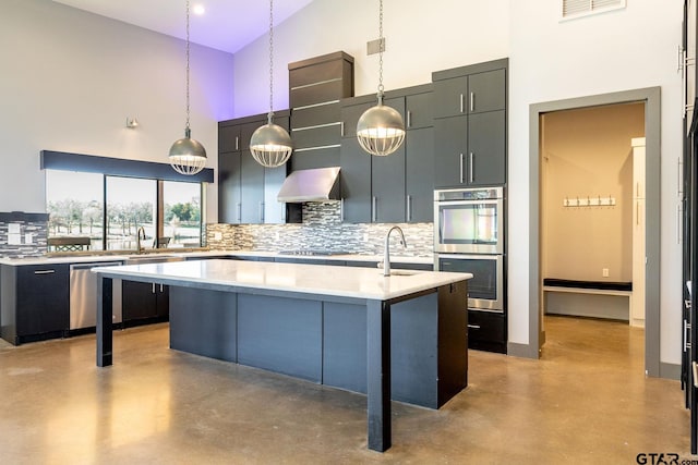 kitchen with light countertops, appliances with stainless steel finishes, a kitchen island with sink, a sink, and concrete floors