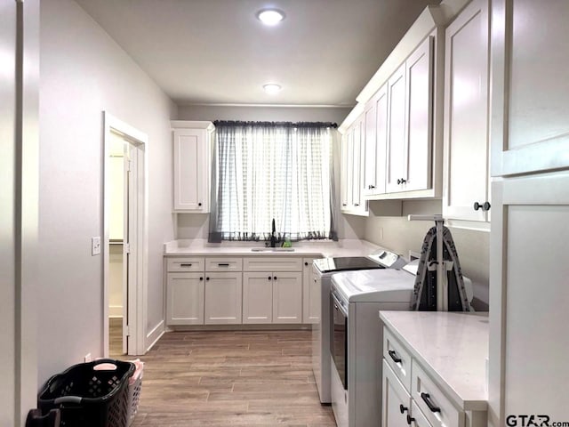 clothes washing area with sink, washer and clothes dryer, light hardwood / wood-style floors, and cabinets