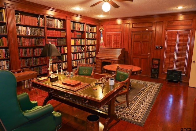 home office with dark wood-type flooring, a textured ceiling, ornamental molding, ceiling fan, and built in features