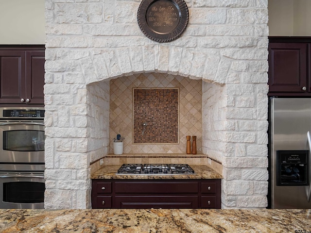 kitchen featuring light stone counters, decorative backsplash, dark brown cabinetry, and stainless steel appliances