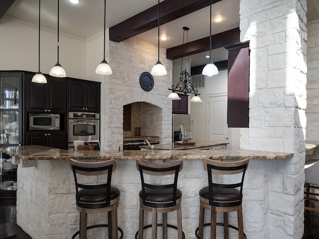 kitchen featuring beamed ceiling, appliances with stainless steel finishes, decorative light fixtures, and a breakfast bar