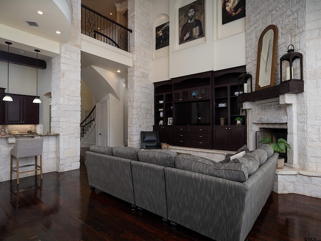 living room with a high ceiling, dark hardwood / wood-style floors, a stone fireplace, and decorative columns