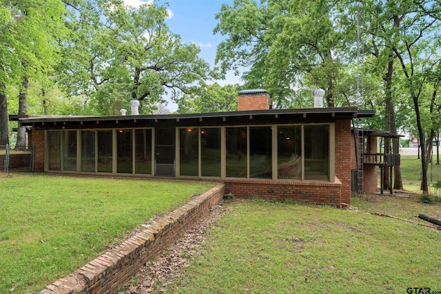 back of property featuring a chimney, a sunroom, a yard, and brick siding