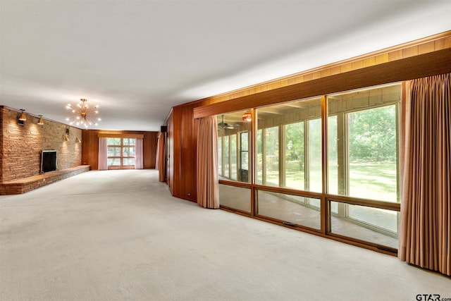 unfurnished living room featuring a fireplace, a notable chandelier, wood walls, and light carpet