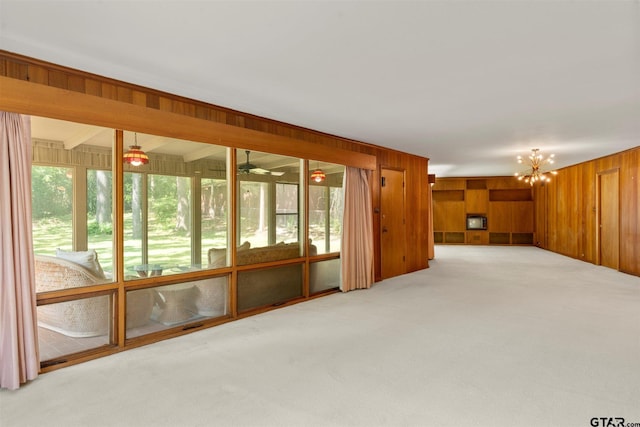 unfurnished living room with ceiling fan with notable chandelier, wooden walls, carpet, and a healthy amount of sunlight