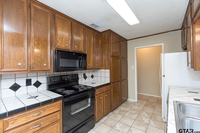 kitchen featuring visible vents, backsplash, tile counters, brown cabinets, and black appliances