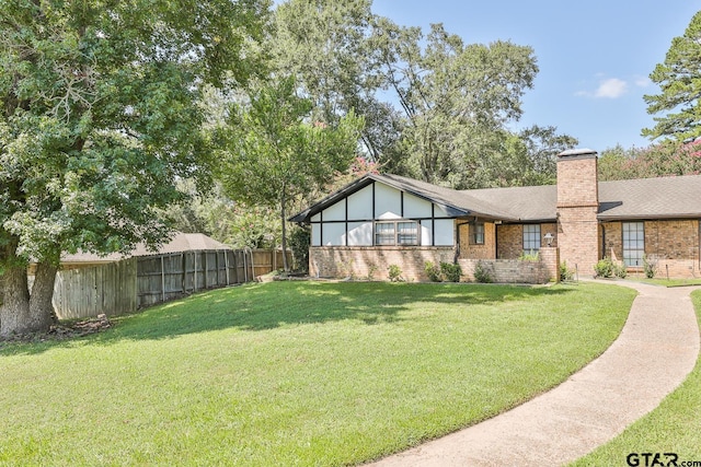 view of front of home featuring brick siding, fence, a chimney, and a front lawn