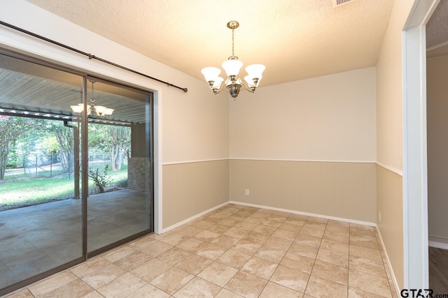 unfurnished room featuring a chandelier, a wainscoted wall, and a textured ceiling