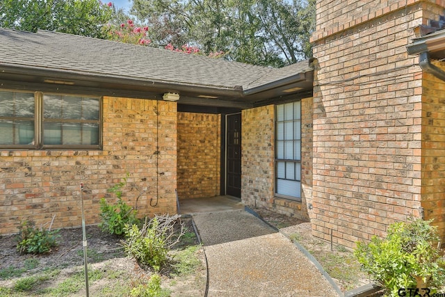 view of exterior entry featuring brick siding and roof with shingles