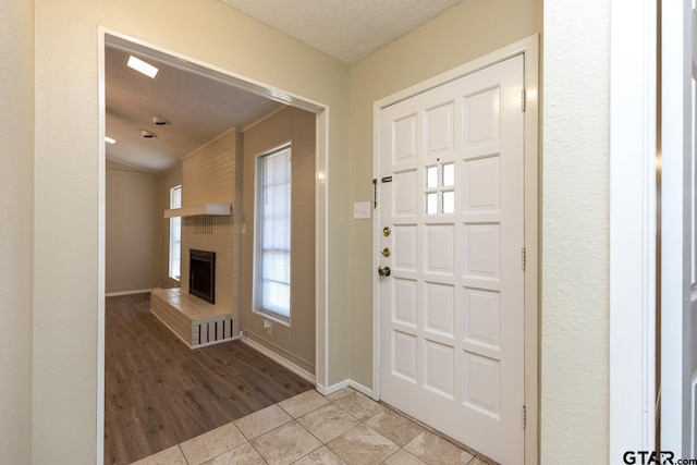 tiled entrance foyer featuring a textured ceiling, a fireplace, and baseboards