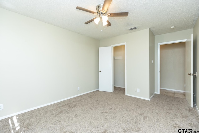 unfurnished bedroom with carpet, visible vents, a spacious closet, a textured ceiling, and baseboards