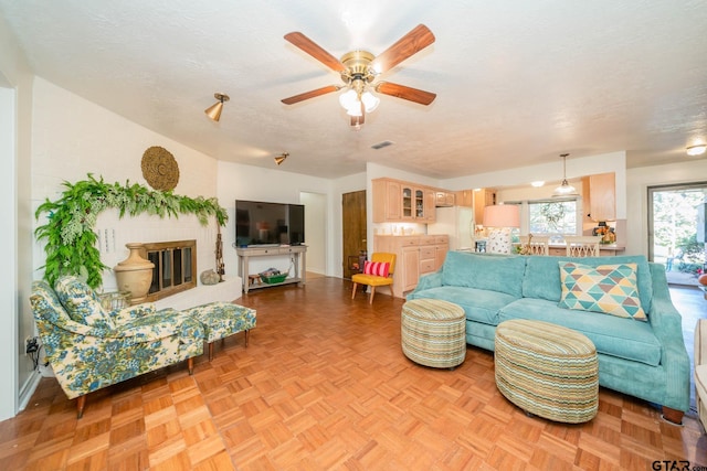 living room with light parquet flooring, a brick fireplace, ceiling fan, and a textured ceiling