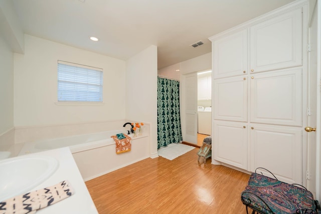 bathroom with hardwood / wood-style flooring, vanity, washer / clothes dryer, and plus walk in shower