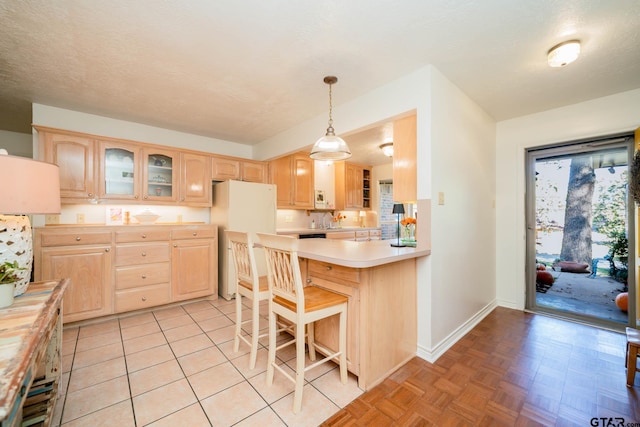 kitchen featuring decorative light fixtures, light brown cabinets, white refrigerator, a kitchen breakfast bar, and kitchen peninsula