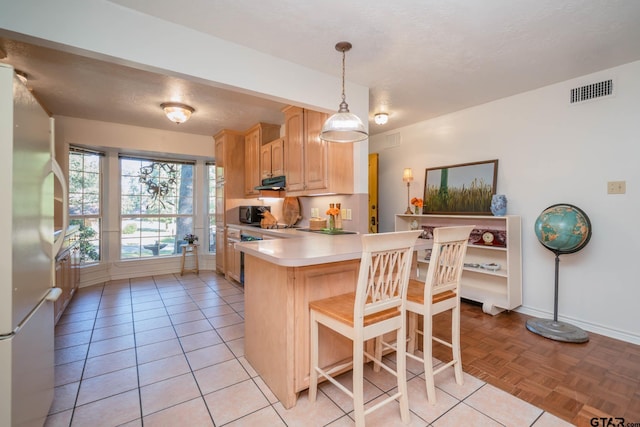 kitchen with a breakfast bar, hanging light fixtures, light brown cabinets, fridge, and kitchen peninsula