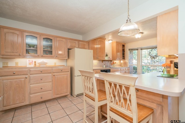 kitchen with light tile patterned floors, white fridge, a textured ceiling, decorative light fixtures, and light brown cabinets