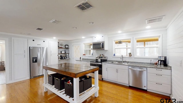 kitchen with sink, light stone counters, light wood-type flooring, appliances with stainless steel finishes, and white cabinets